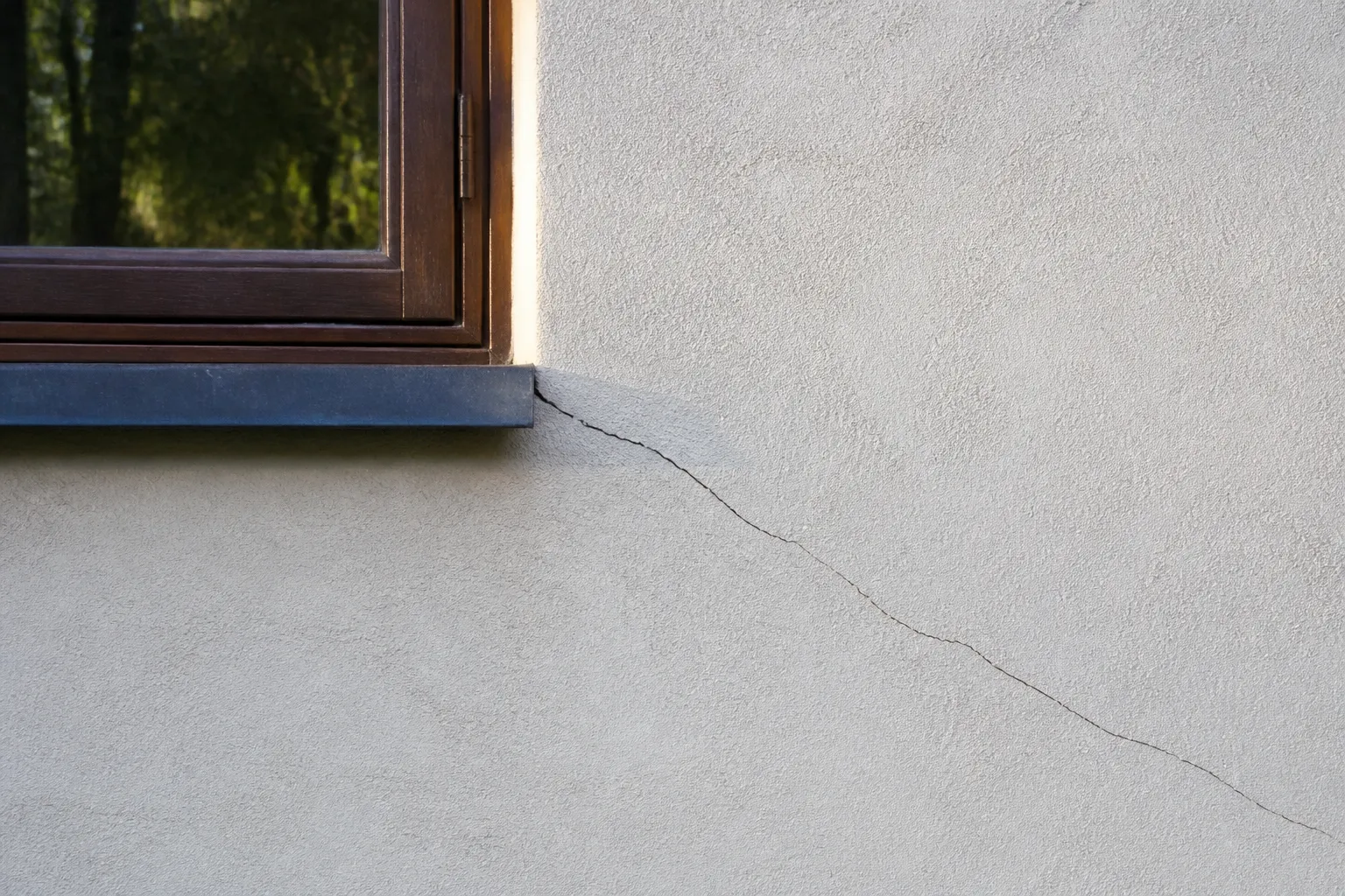 Fissure sur un mur extérieur enduit près d’une fenêtre