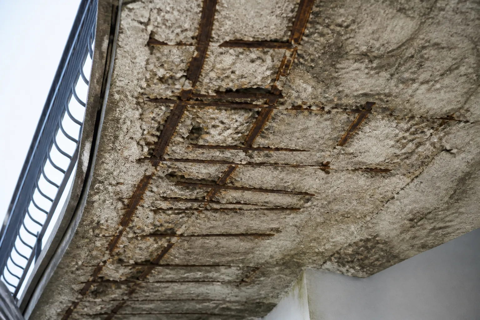 Sous-face de balcon en béton avec éclats et armatures apparentes