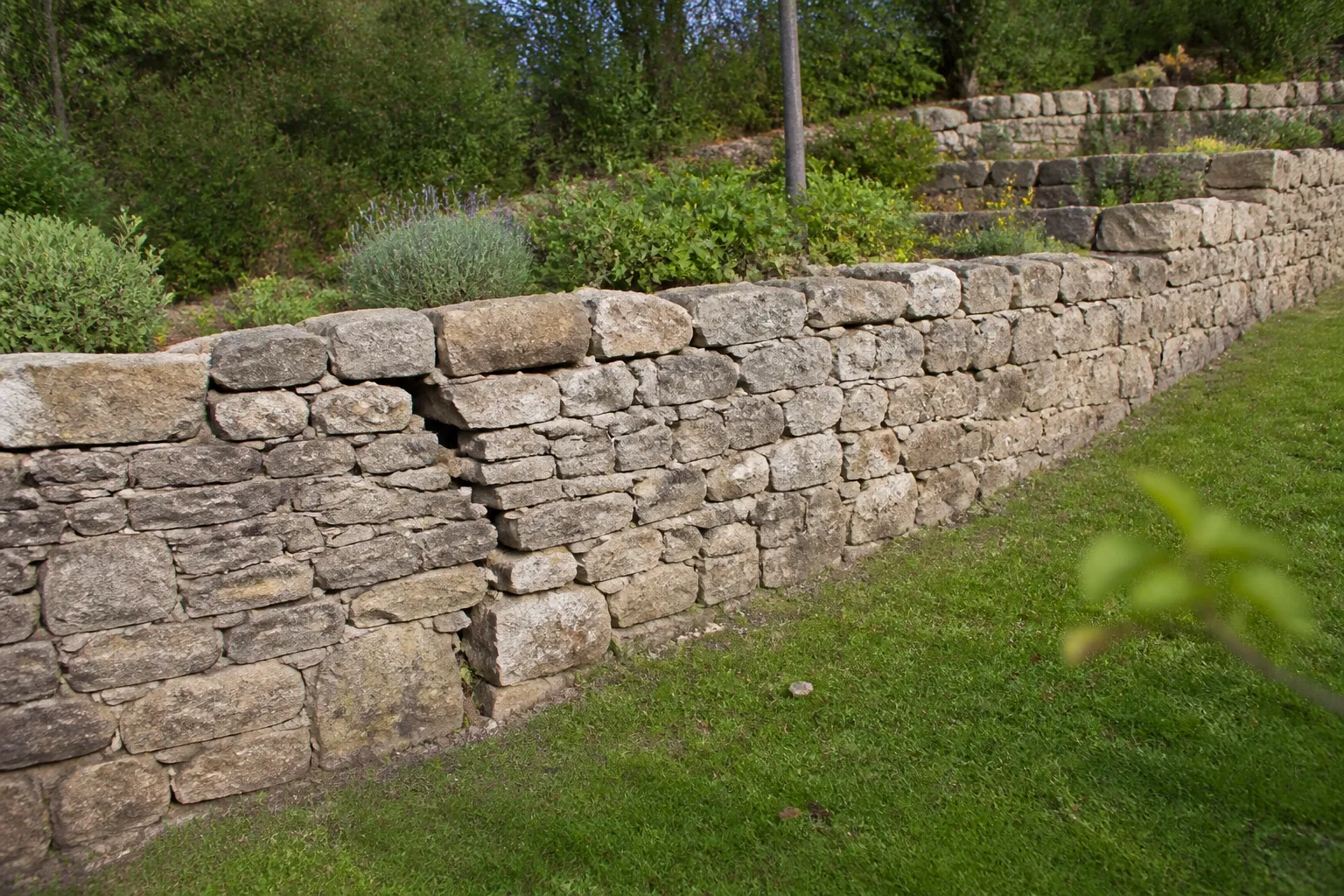 Mur de soutènement en pierre avec fissure dans un jardin en pente