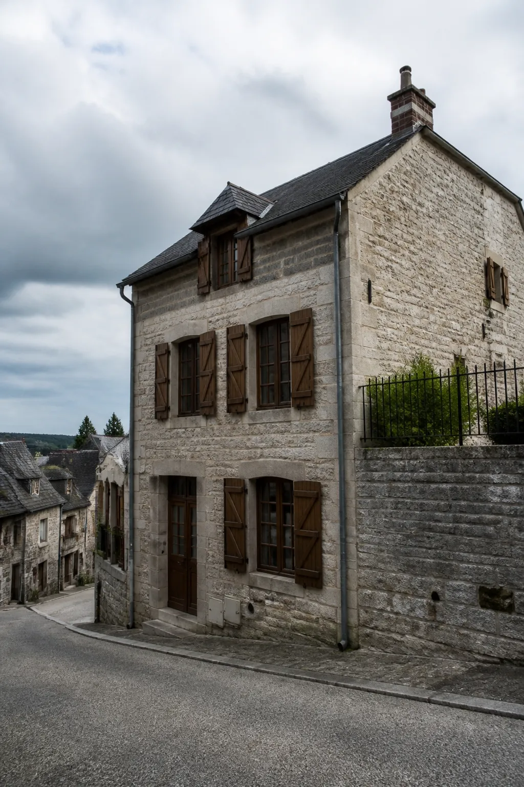 Maison de ville en pierre grise avec toiture sombre dans une rue en pente