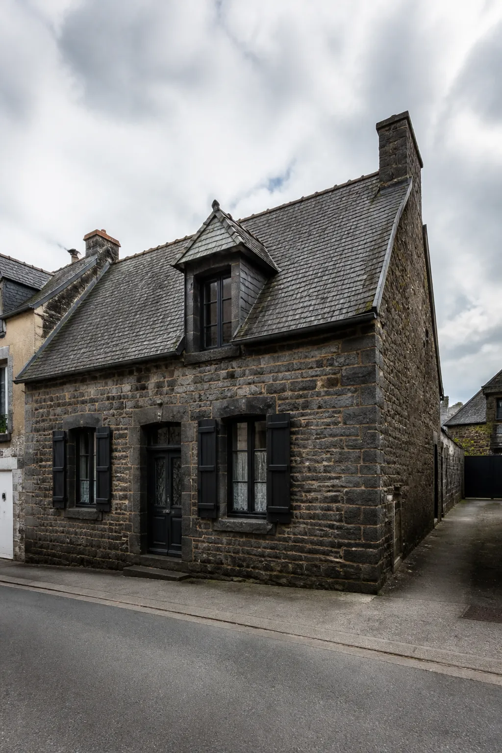 Maison de bourg en pierre sombre avec toit pentu dans une rue calme