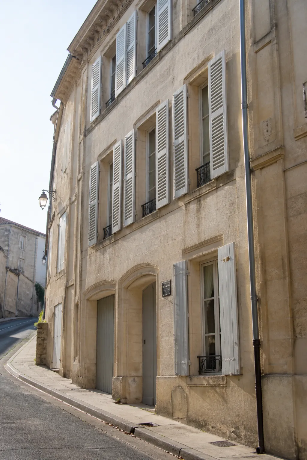 Immeuble ancien en pierre claire dans une rue en pente d’une ville de Charente
