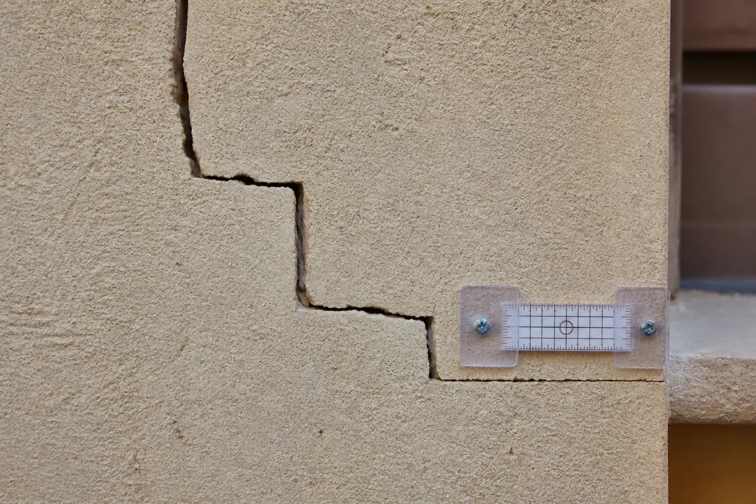 Fissure en escalier sur un mur extérieur enduit, examinée de près