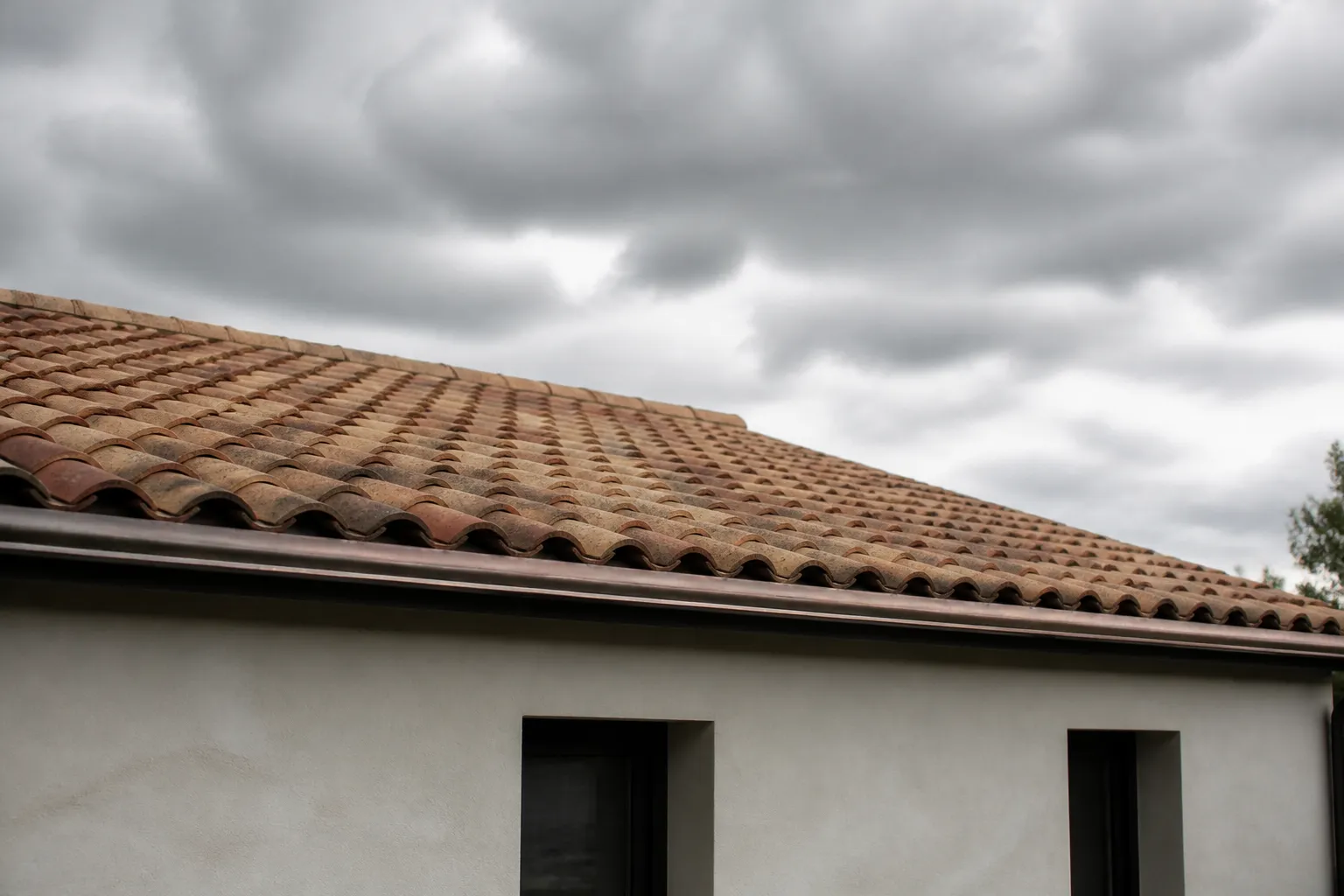 Toiture en tuiles et gouttière sous un ciel de vent