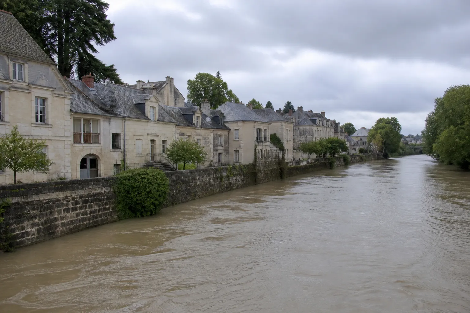 Rivière en crue lente longeant des maisons en pierre