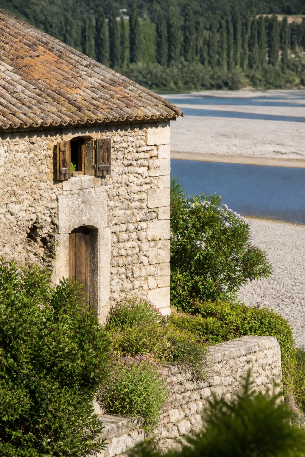 Maison en pierre près d’une rivière à galets bordée d’arbres
