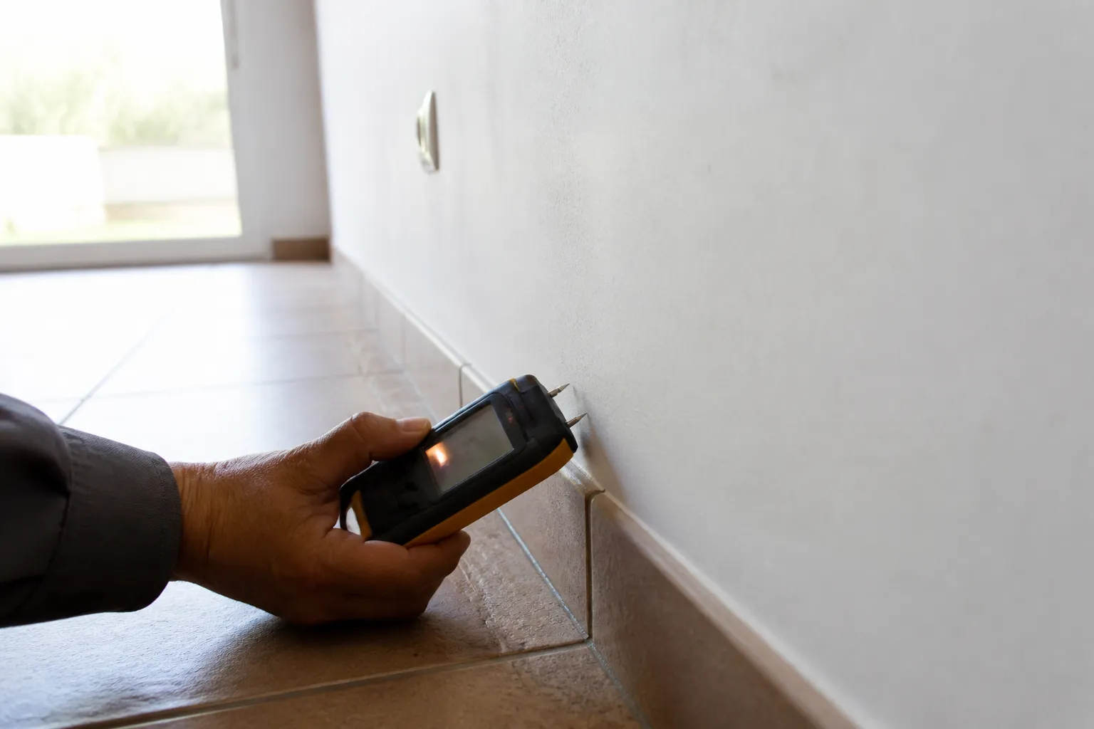 Expert mesurant l’humidité au pied d’un mur de séjour en rez-de-chaussée