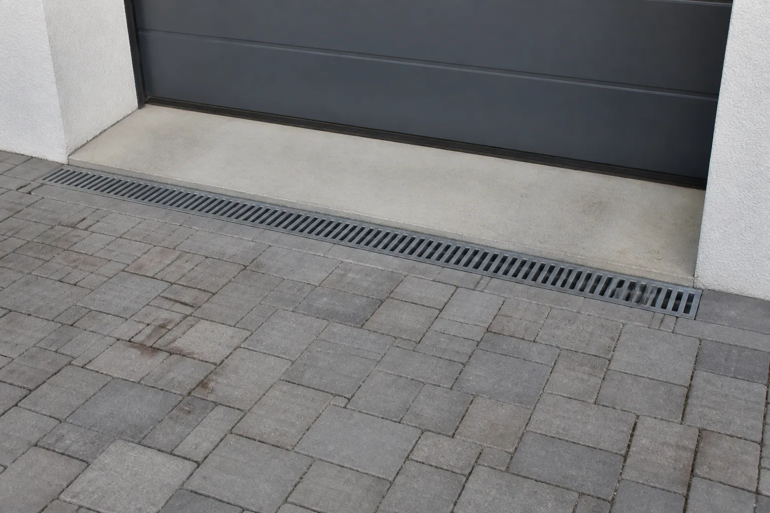 Grille d’évacuation des eaux pluviales devant l’entrée d’une maison en pente