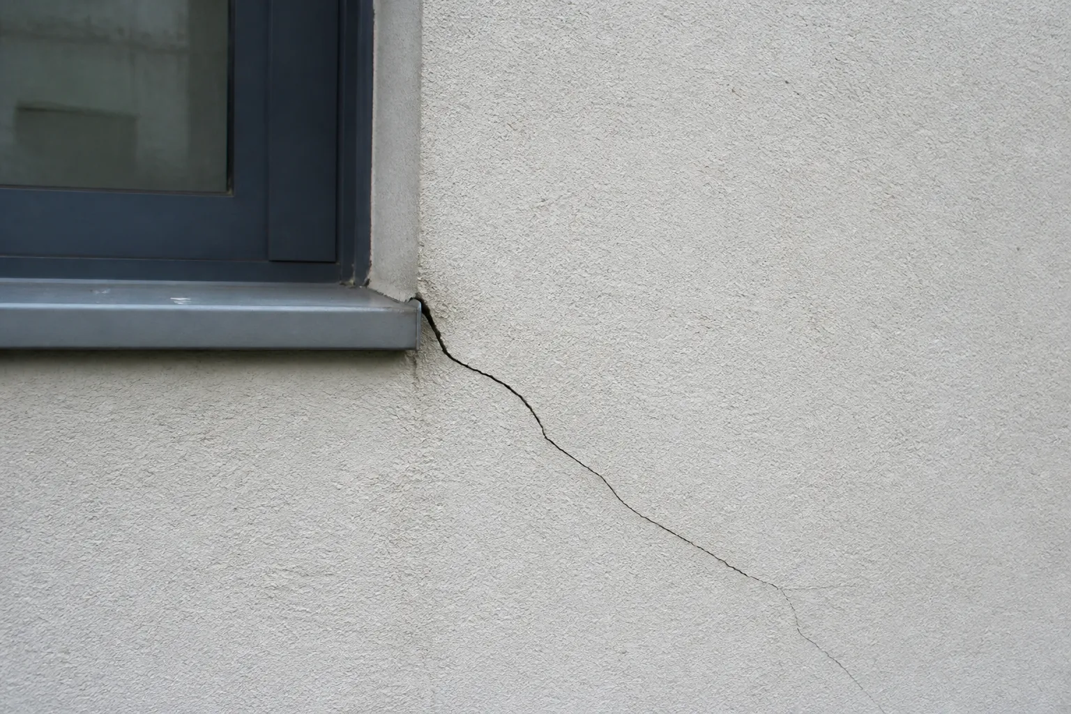 Fissure oblique au-dessus d’une fenêtre sur une façade enduite