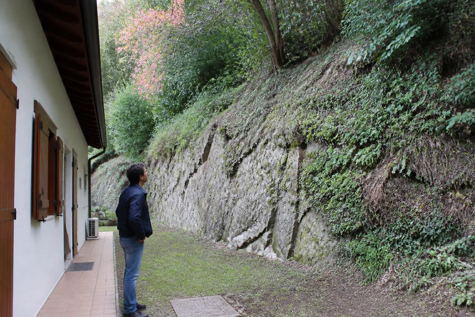 Expert en bâtiment observant un talus rocheux derrière une maison