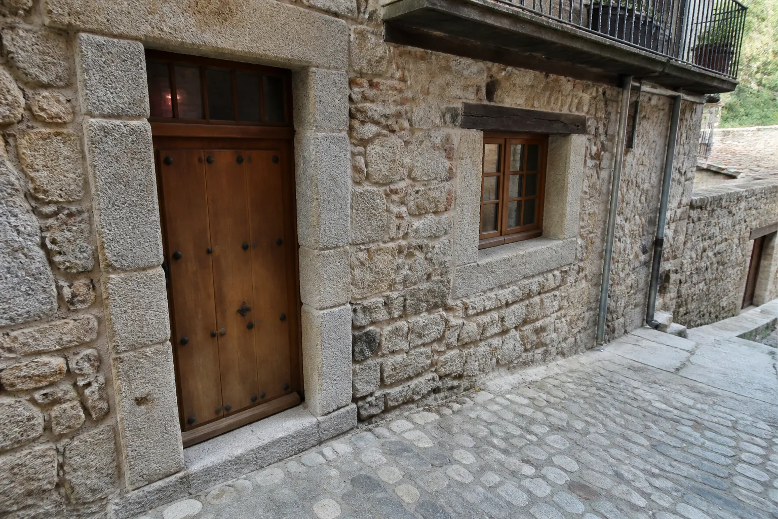 Rez-de-chaussée ancien avec porte en bois et seuil en pierre sur une rue en pente