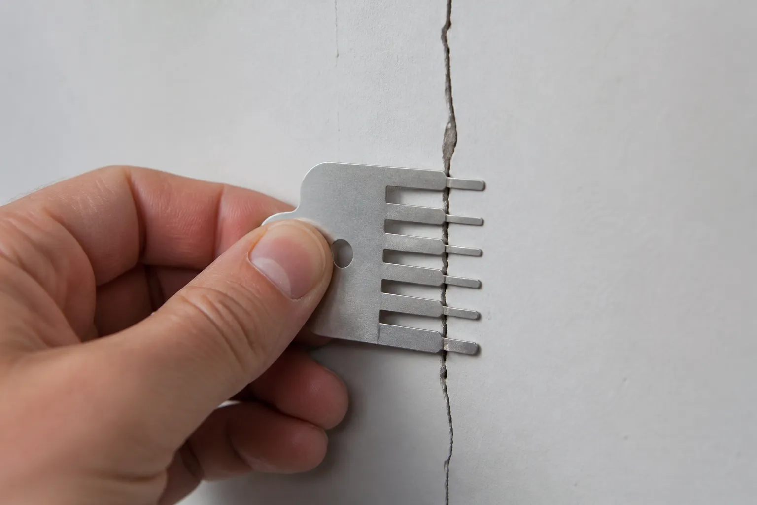 Expert en bâtiment mesurant une fissure sur un mur intérieur
