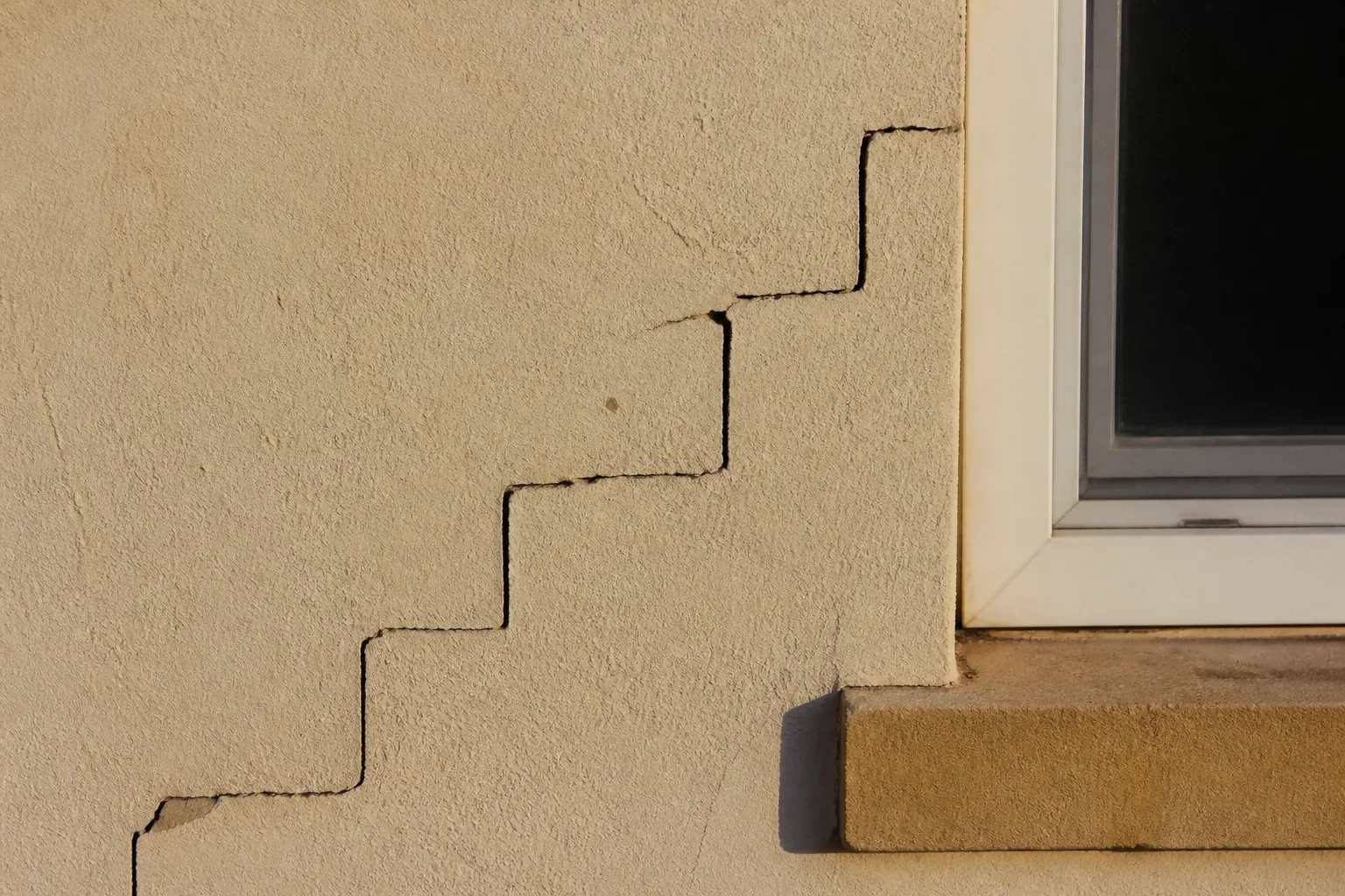 Fissure en escalier sur un mur extérieur enduit