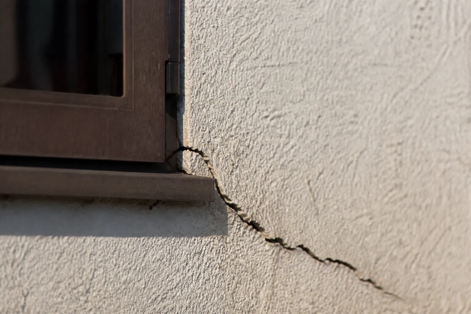 Fissure en biais au-dessus d’une fenêtre sur un mur enduit