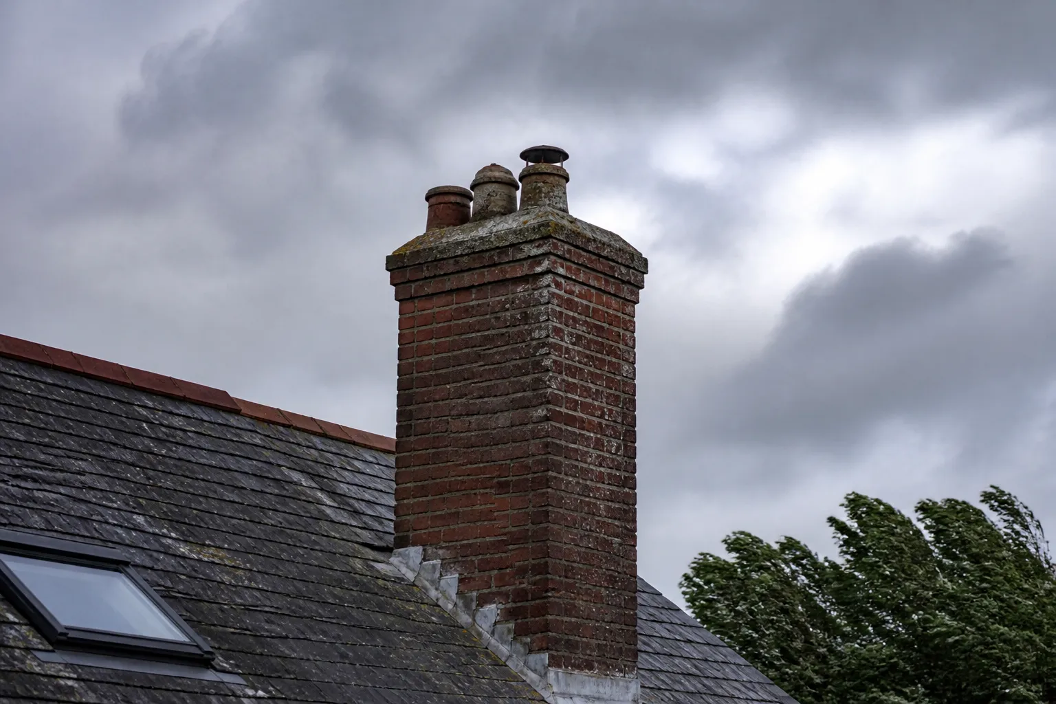 Souche de cheminée et toiture en ardoise sous un ciel venteux