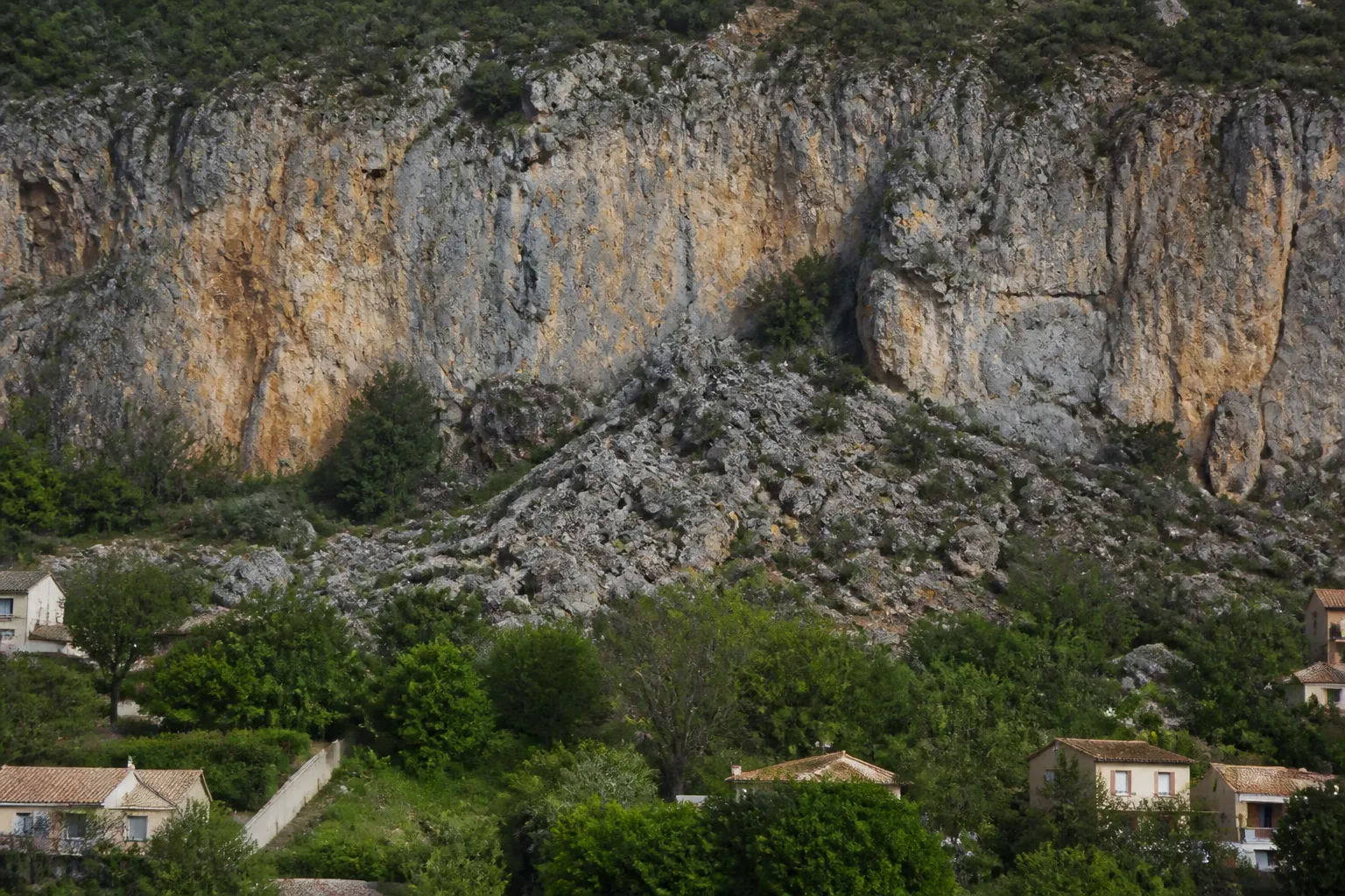 Pied de falaise rocheuse avec éboulis au-dessus de jardins