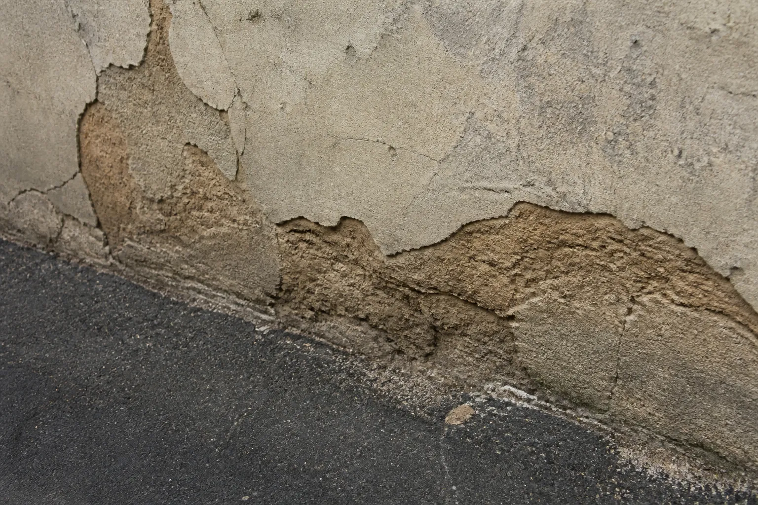 Pied de mur en pisé avec enduit dégradé et terrain remonté