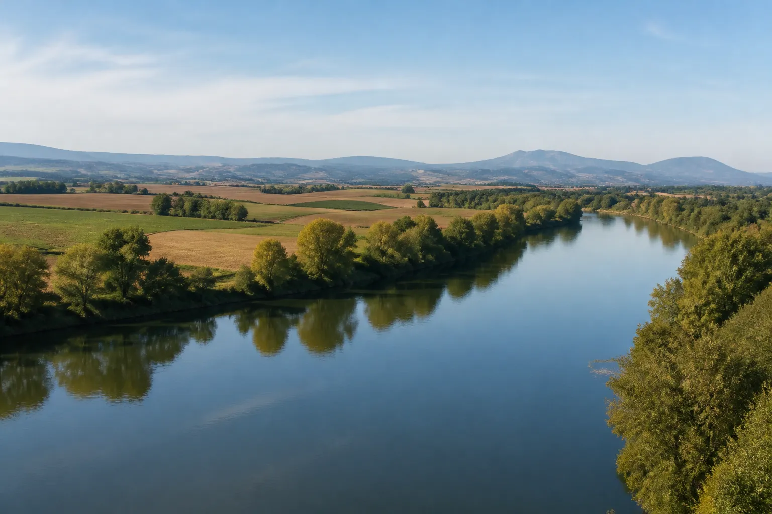 Rivière large bordée d’arbres dans une plaine agricole