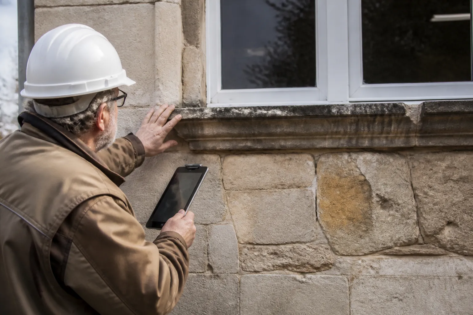 Expert en bâtiment examinant une façade avec une tablette