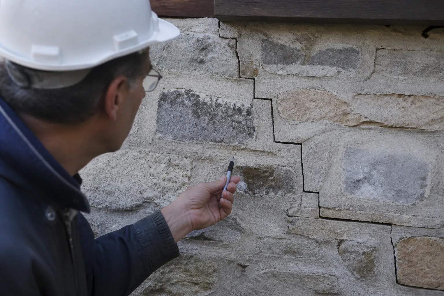 Expert observant une fissure en escalier sur un mur extérieur