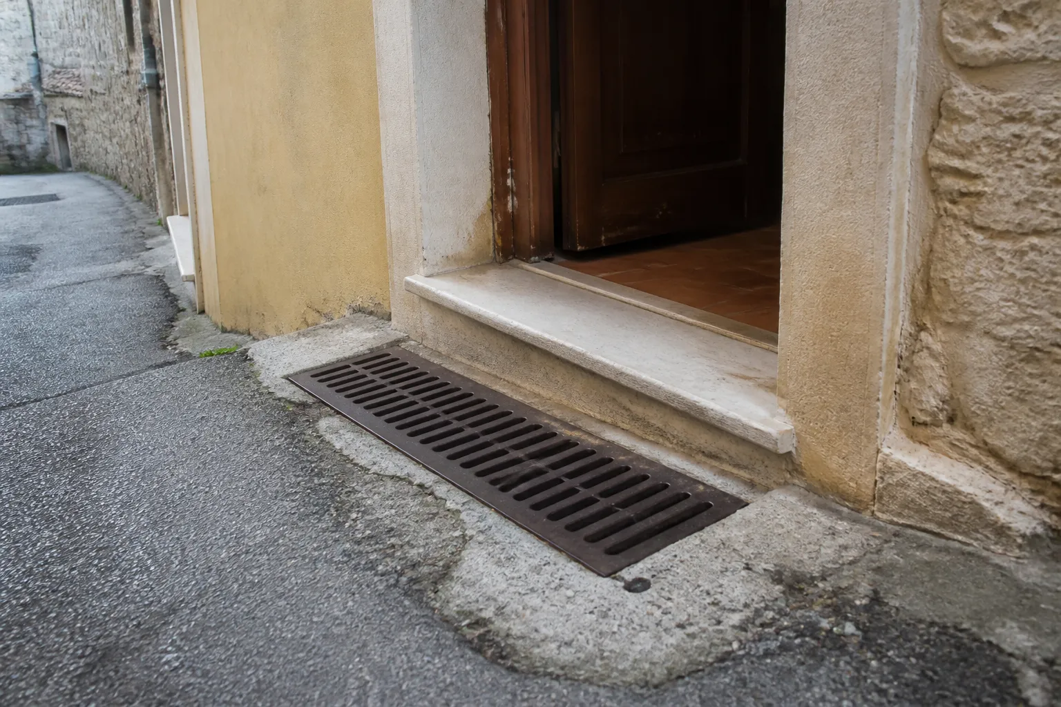 Seuil de porte et grille d’évacuation au bas d’une rue en pente