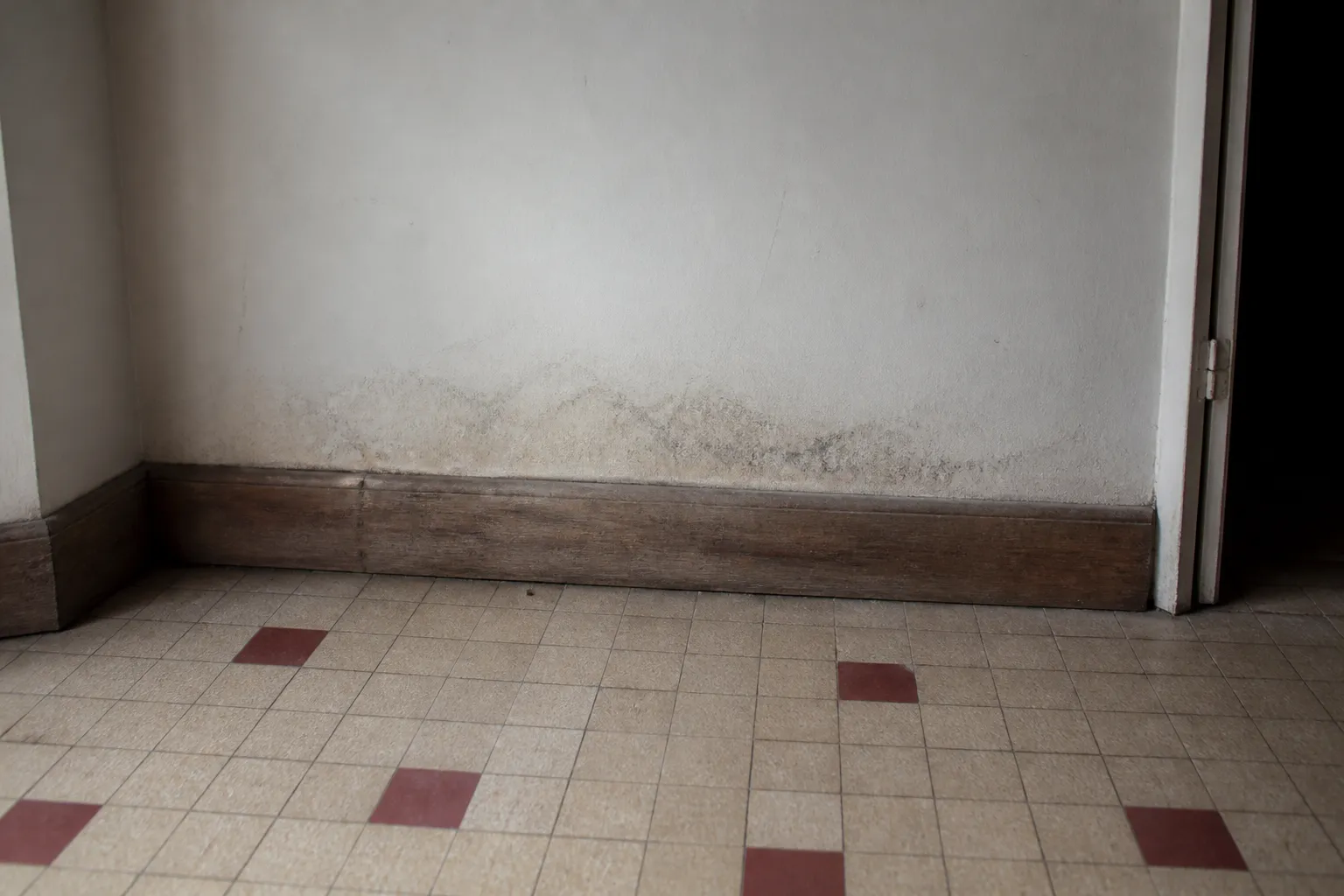 Pied de mur intérieur avec traces d’humidité et plinthe ancienne