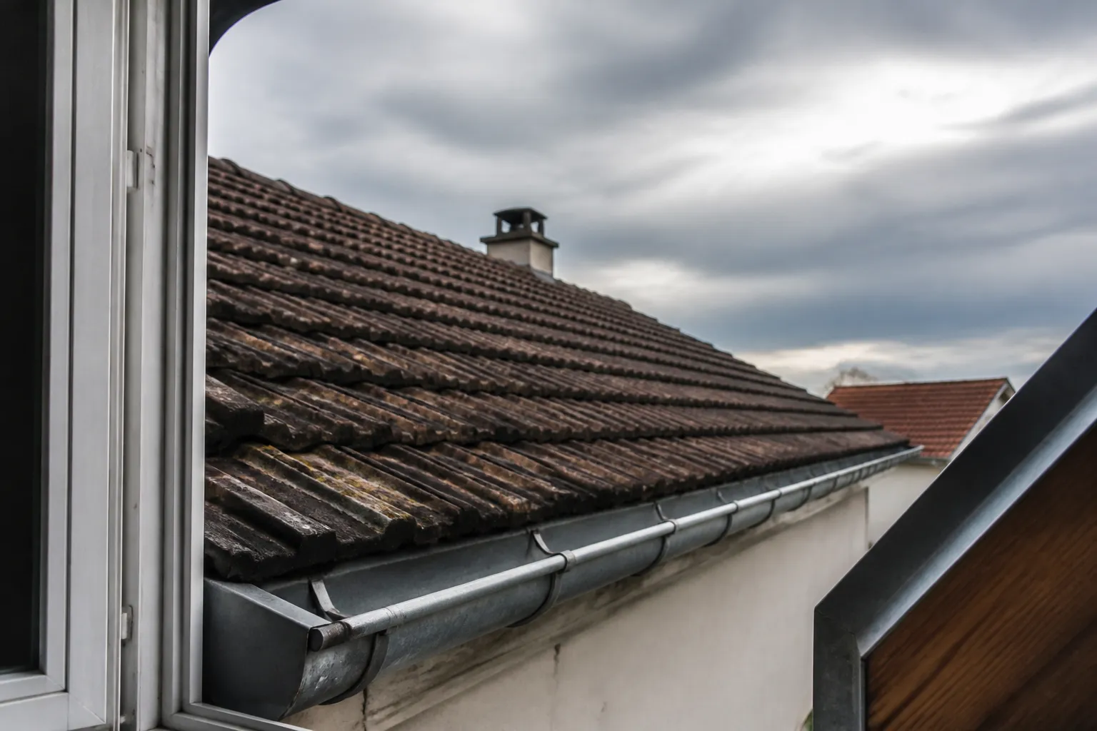 Toiture en tuiles et chéneau vus depuis une lucarne