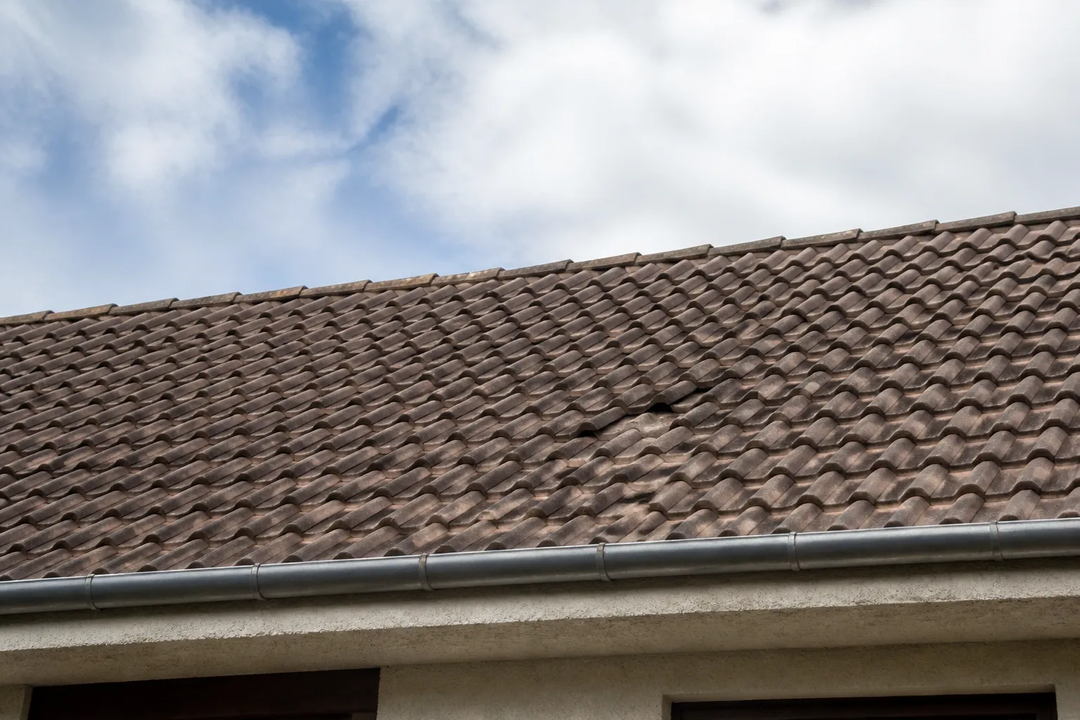 Toiture de tuiles avec quelques tuiles déplacées vue depuis le sol