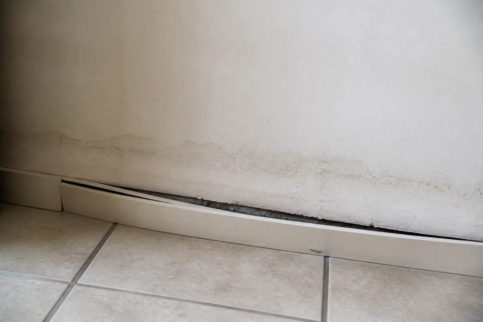 Pied de mur intérieur avec plinthe décollée et trace d’humidité