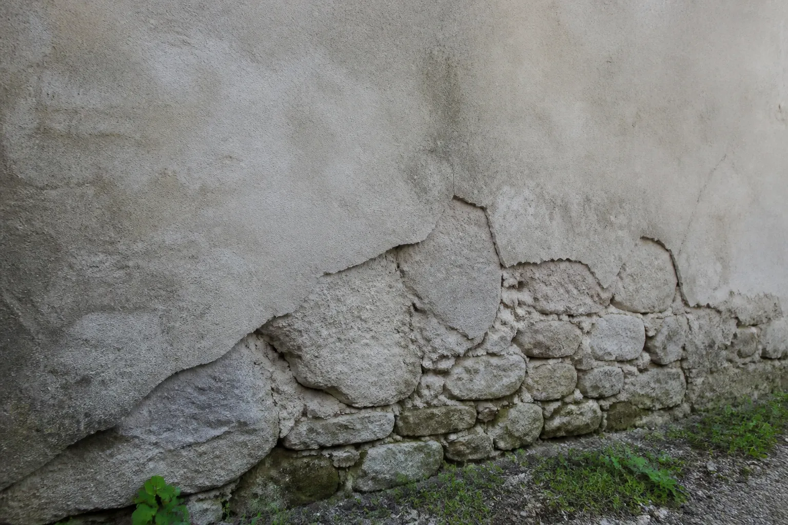 Mur ancien en moellons avec enduit ciment qui se décolle