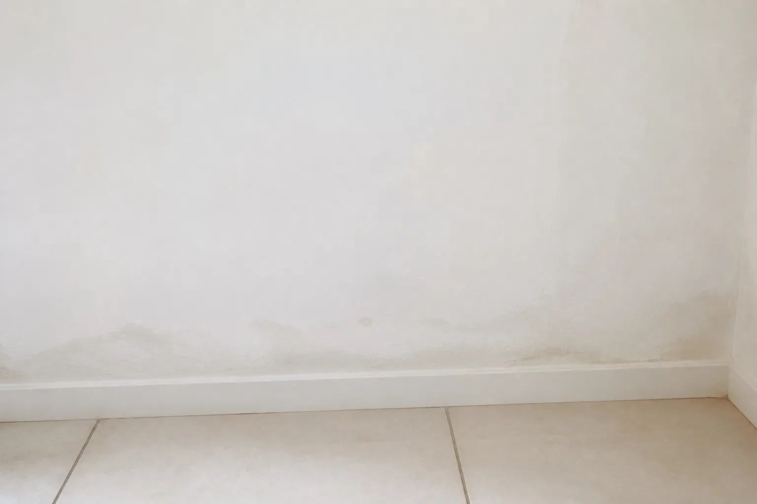 Trace d’humidité récente au bas d’un mur intérieur fraîchement repeint