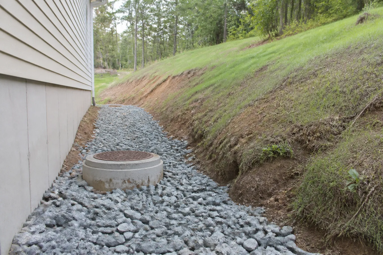 Fossé de drainage et regard en pied de talus derrière une maison