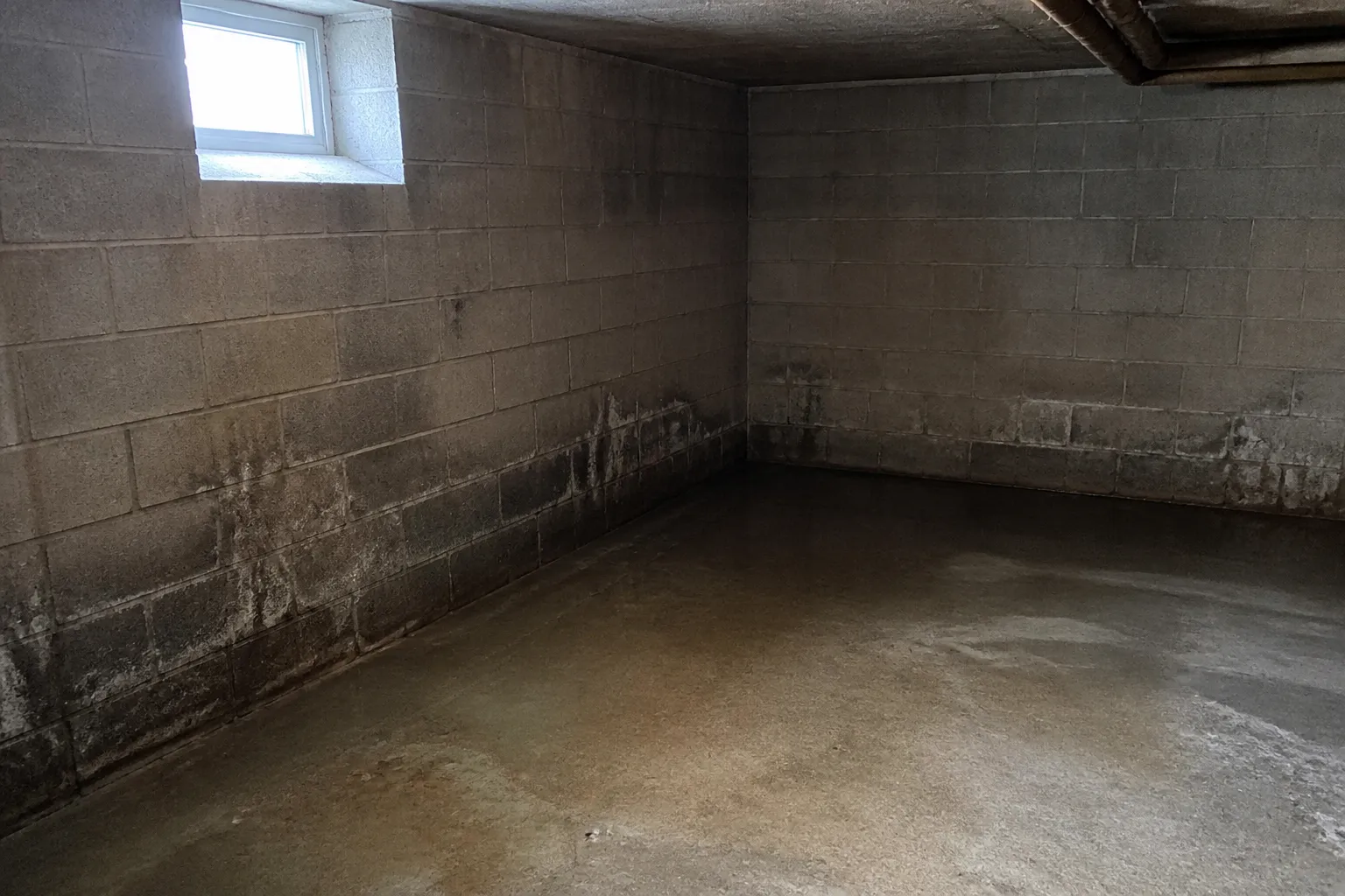 Sous-sol de maison avec mur en parpaings et traces d’humidité au sol