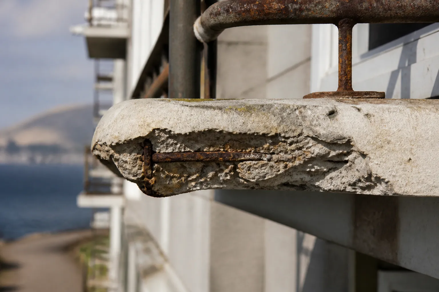 Nez de balcon en béton avec épaufrure et acier apparent sur une façade littorale