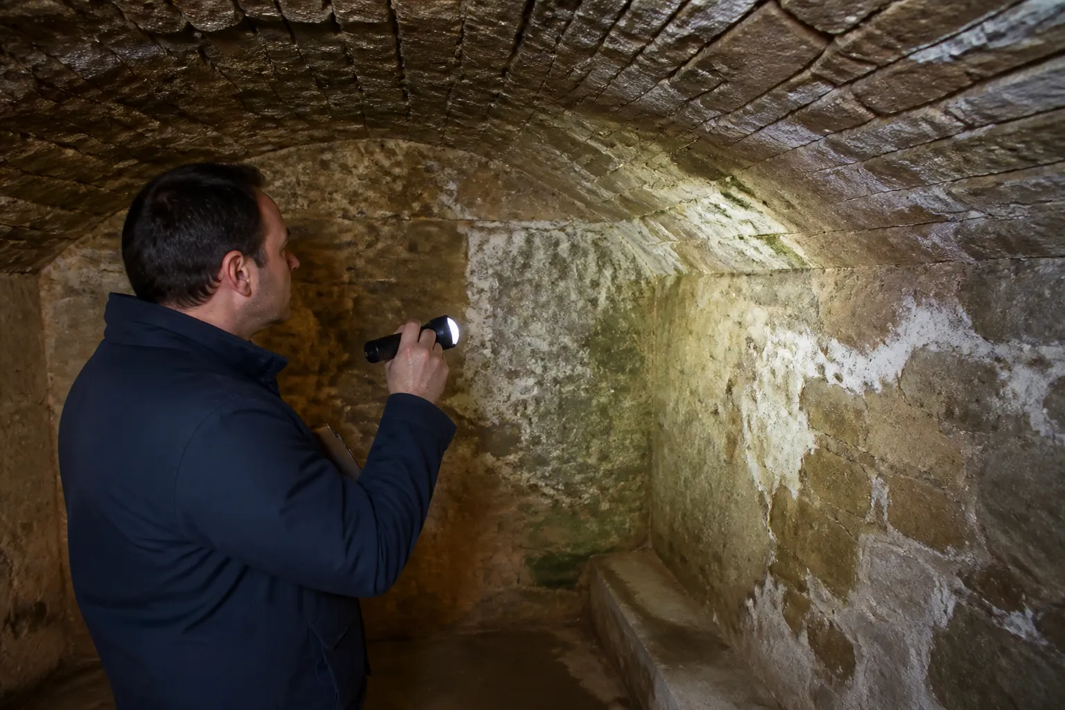 Expert inspectant une cave voûtée avec une lampe torche