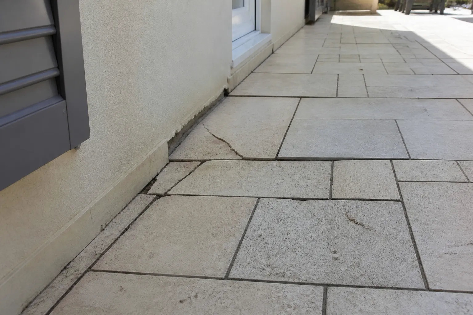 Dallage de terrasse fissuré et affaissé au pied d’une maison