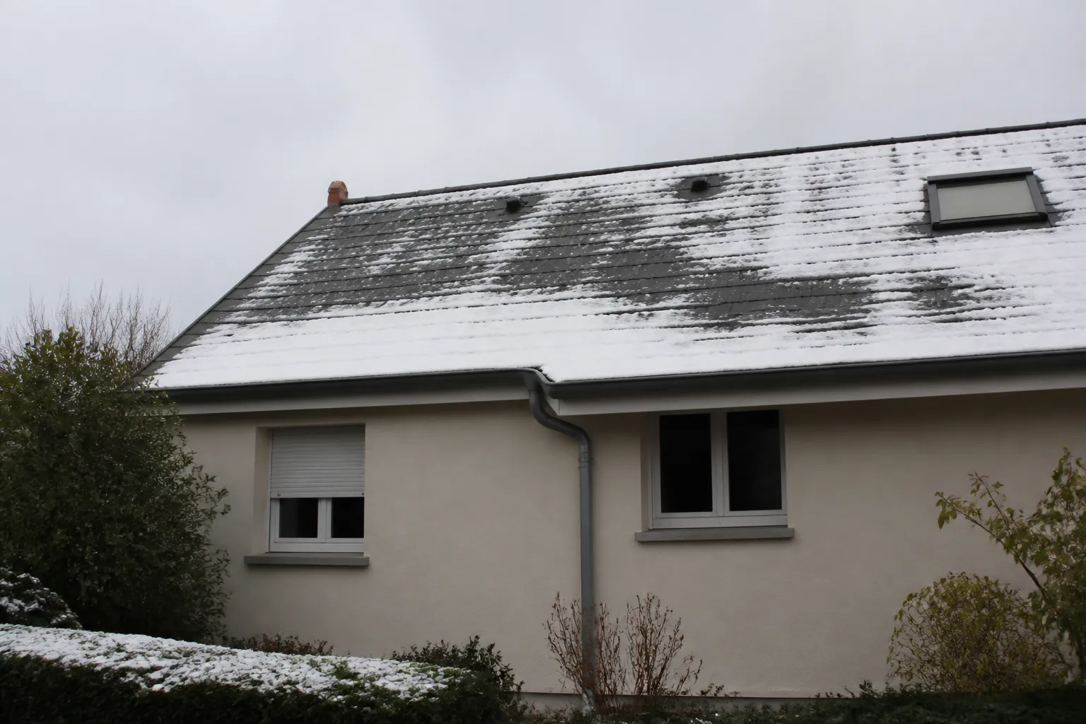 Toiture partiellement couverte de neige vue depuis le jardin
