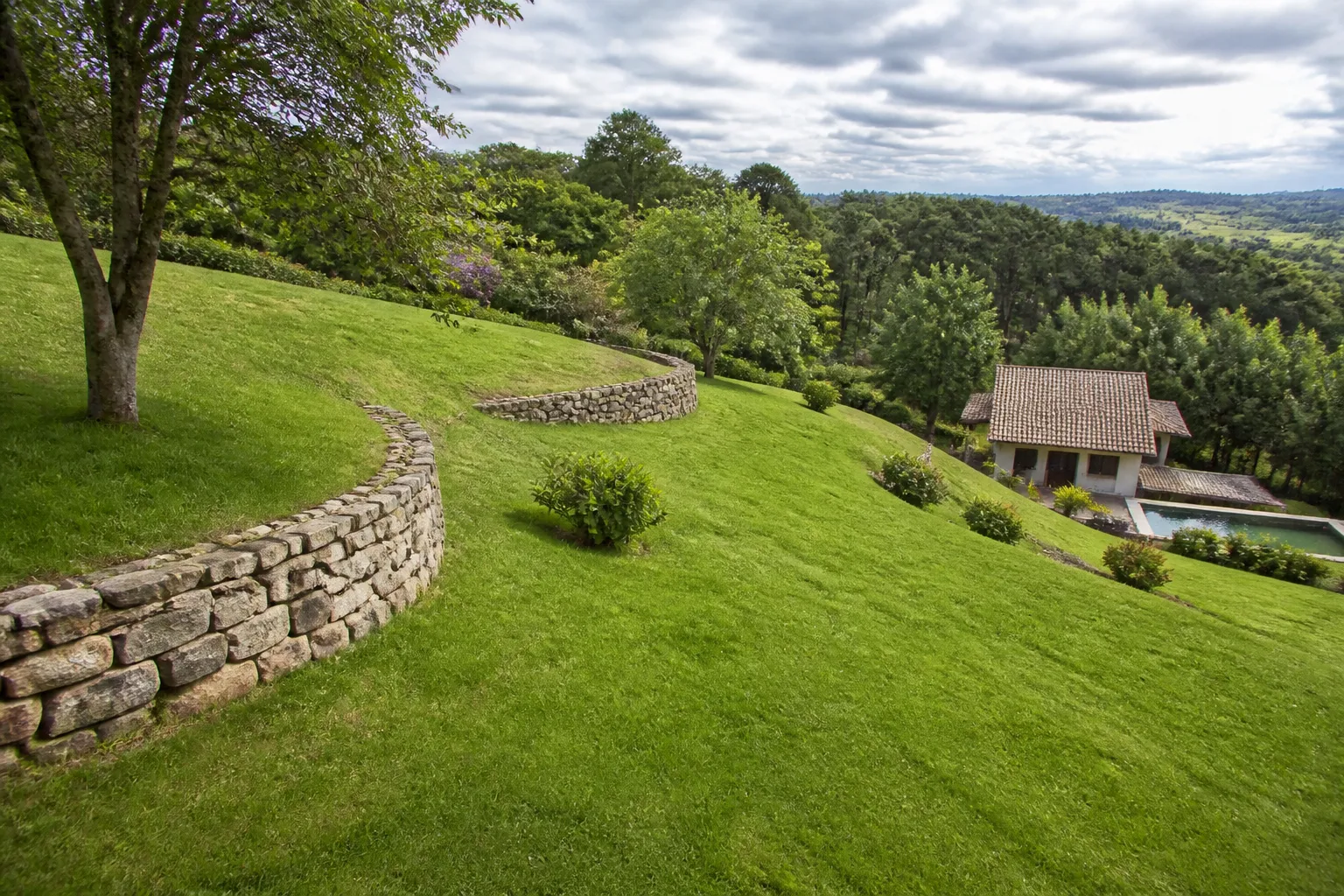 Terrain en pente avec muret et maison en contrebas