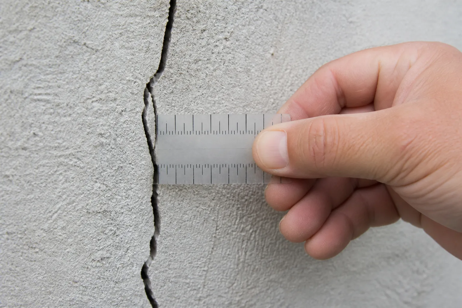Expert en bâtiment mesurant une fissure avec une réglette graduée
