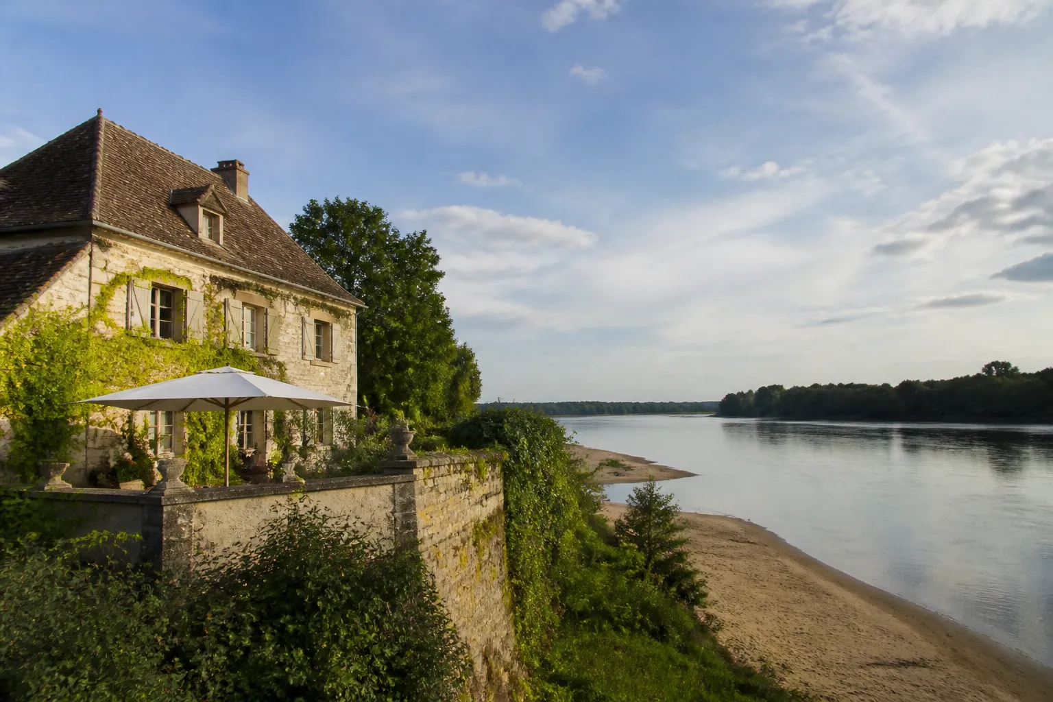 Maison ancienne en bord de fleuve large, vue depuis la berge