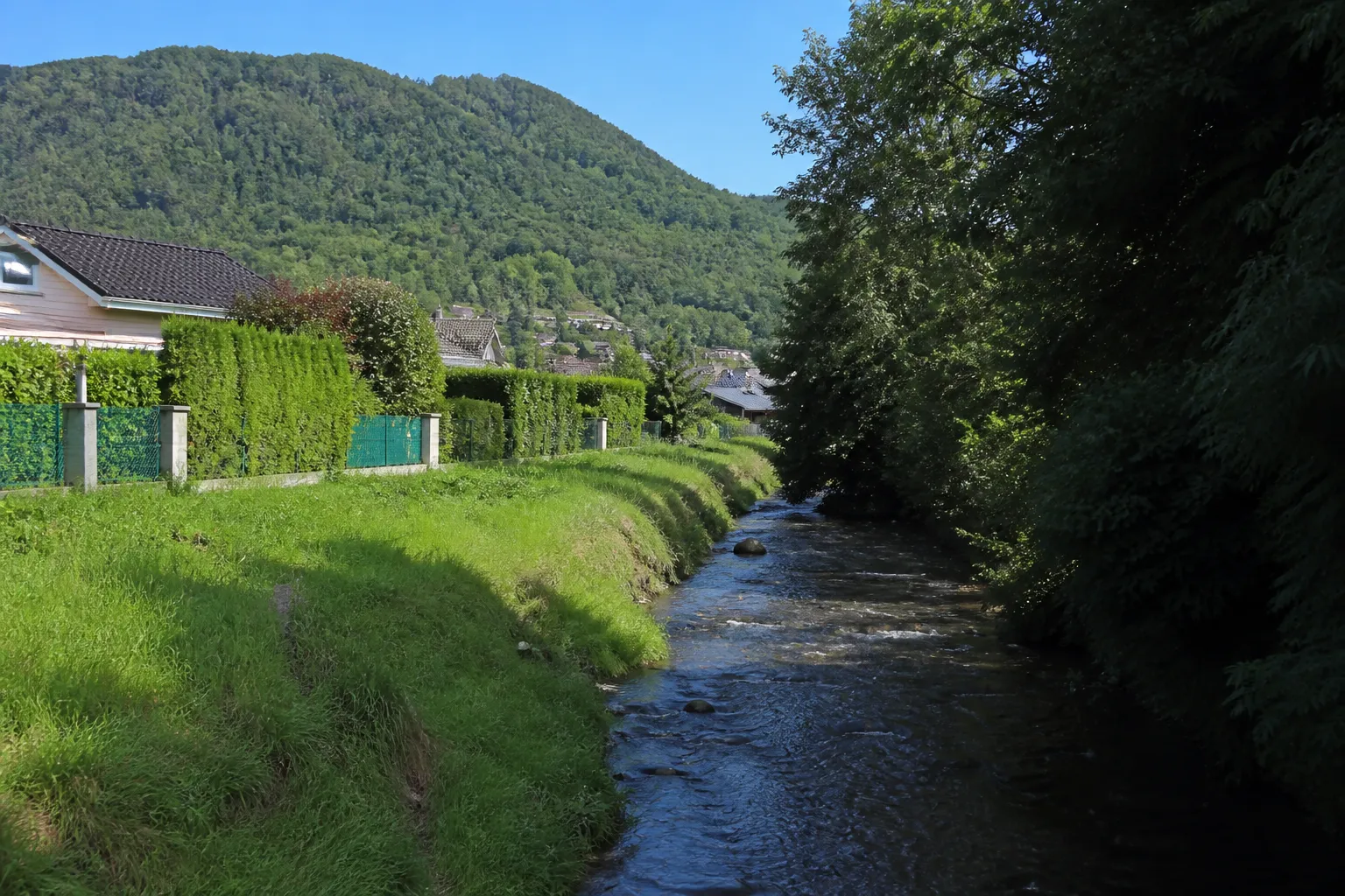 Ruisseau longeant des jardins de maisons au pied des reliefs