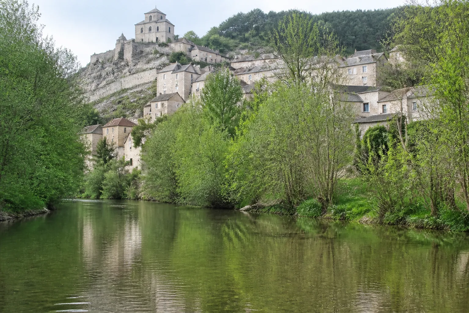 Rivière bordée d’arbres au pied d’un village aux maisons de pierre