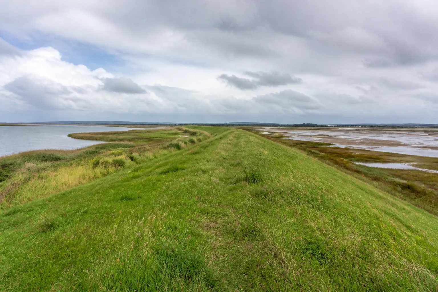 Digue enherbée et marais littoral sous un ciel changeant