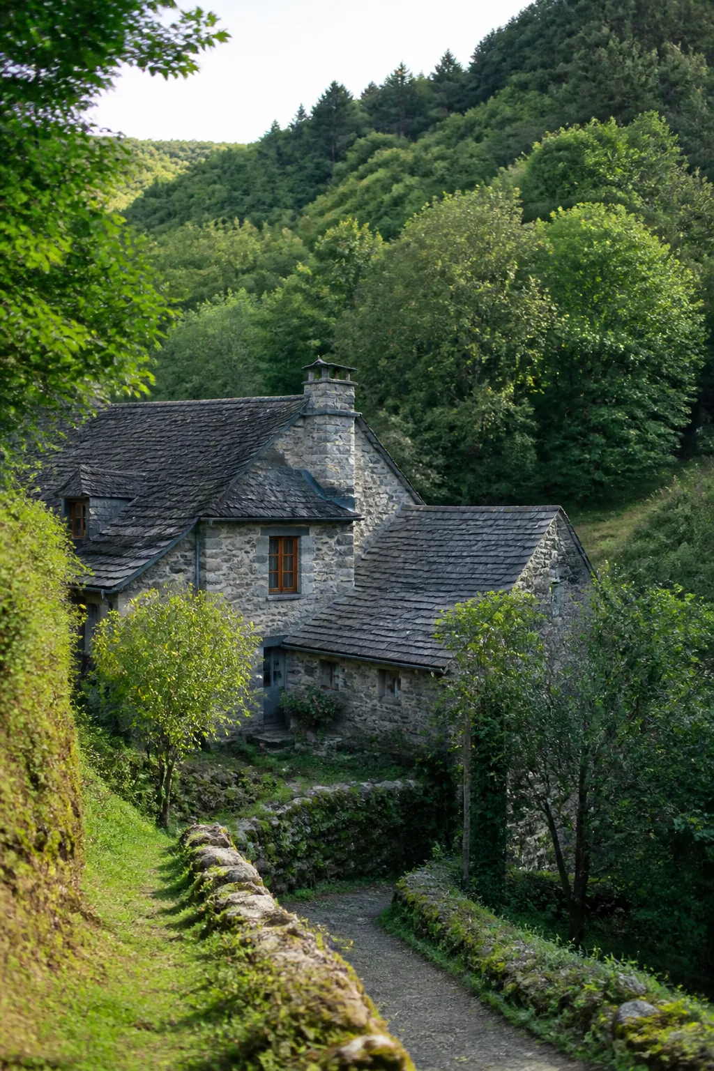 Maison ancienne en pierre avec toiture en ardoise dans une vallée boisée