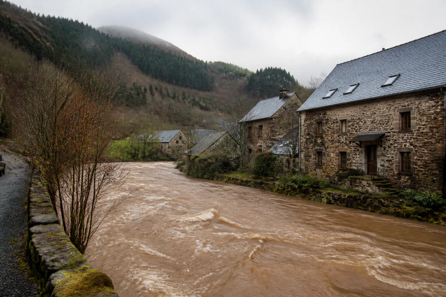 Rivière en crue modérée longeant des maisons de vallée