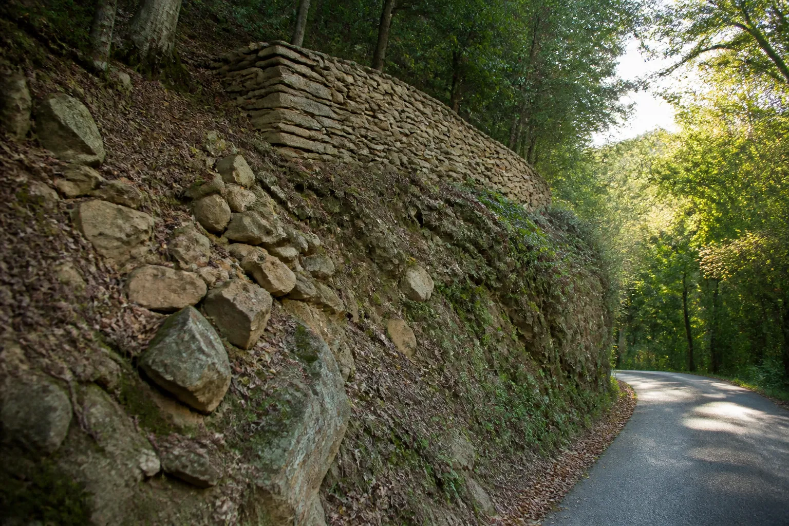 Talus boisé et mur de soutènement en pierre sèche au-dessus d’une route