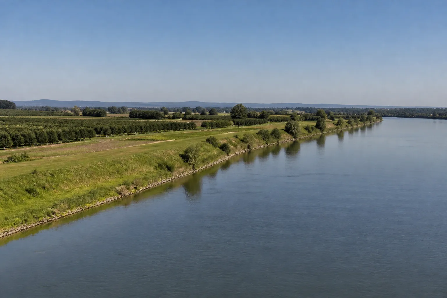 Fleuve large et digue en terre bordant une plaine agricole