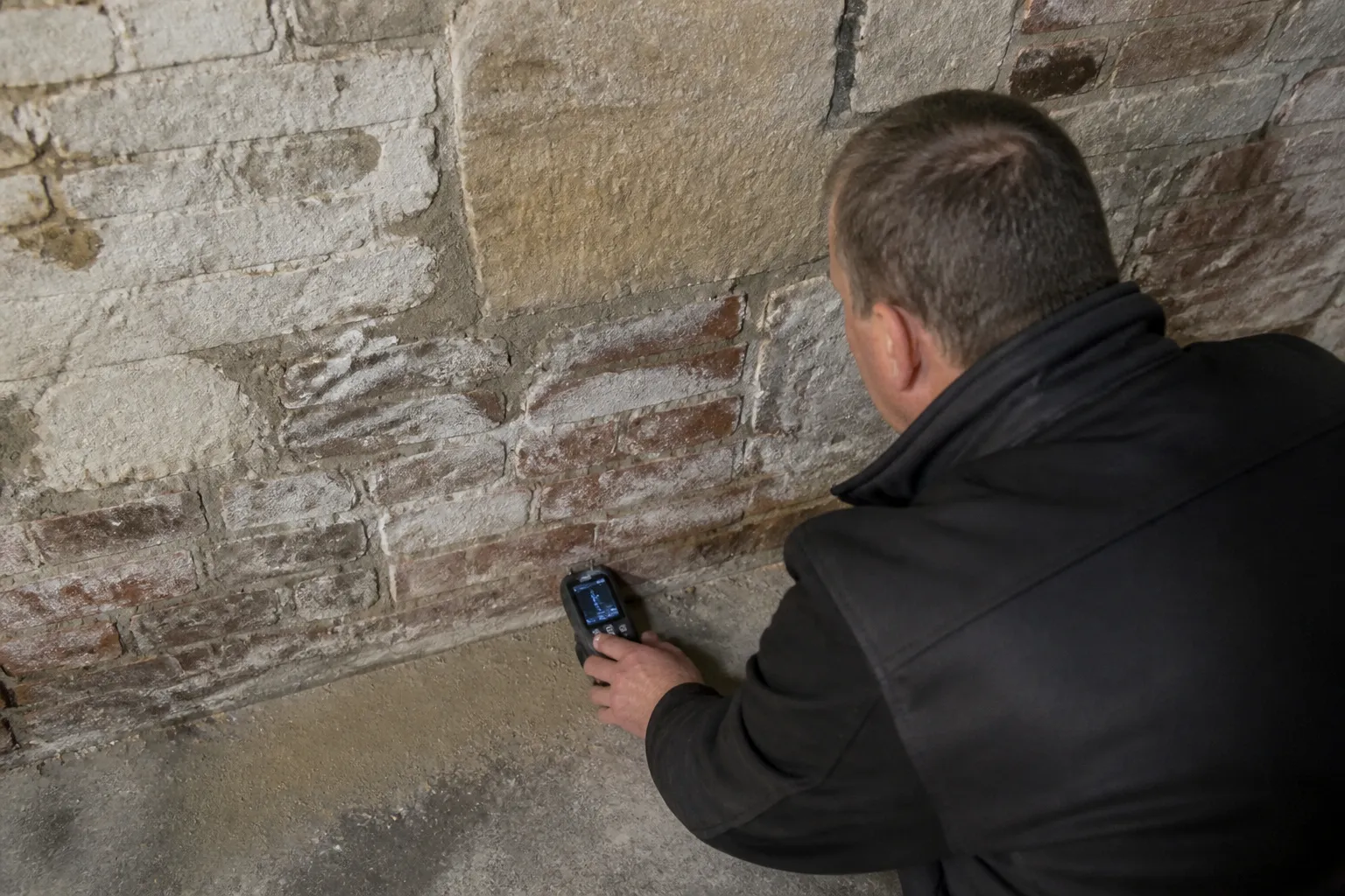 Expert en bâtiment mesurant l’humidité au pied d’un mur dans une maison ancienne