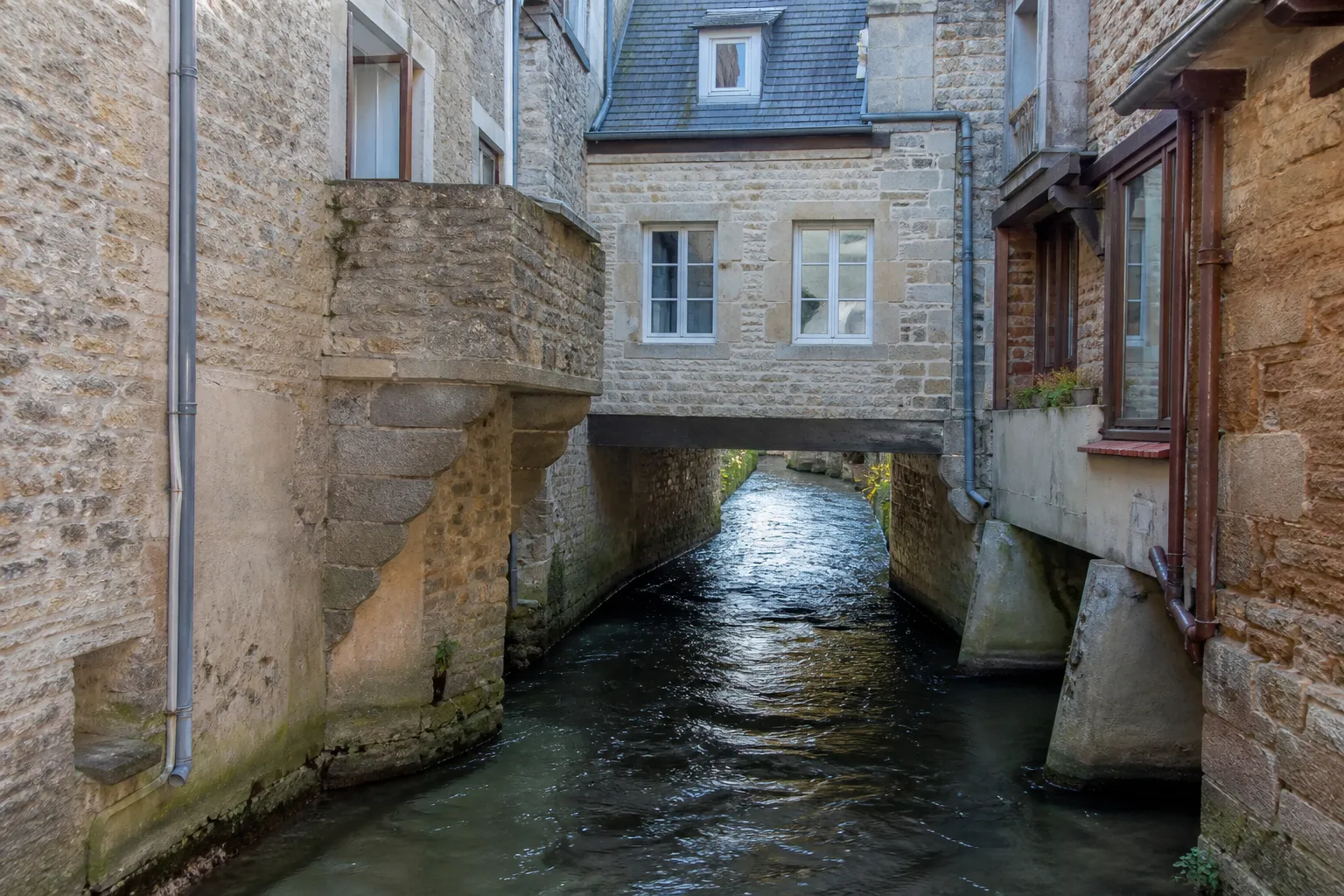 Rivière canalisée passant sous des maisons anciennes en centre-ville