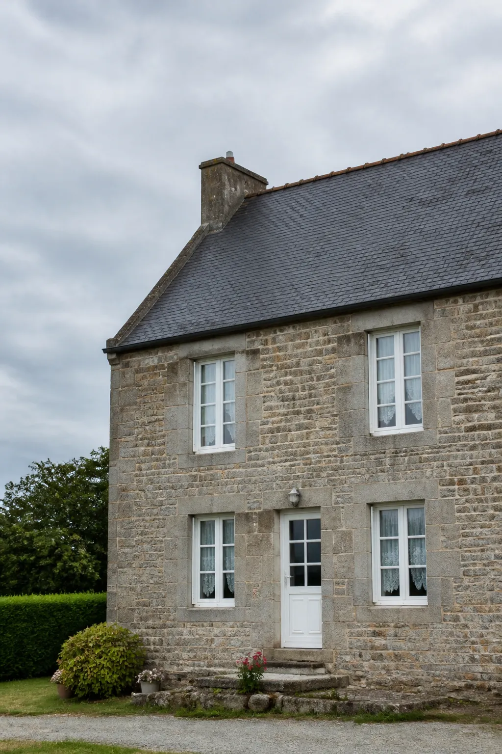 Maison en pierre de granit avec toiture en ardoise sous un ciel nuageux
